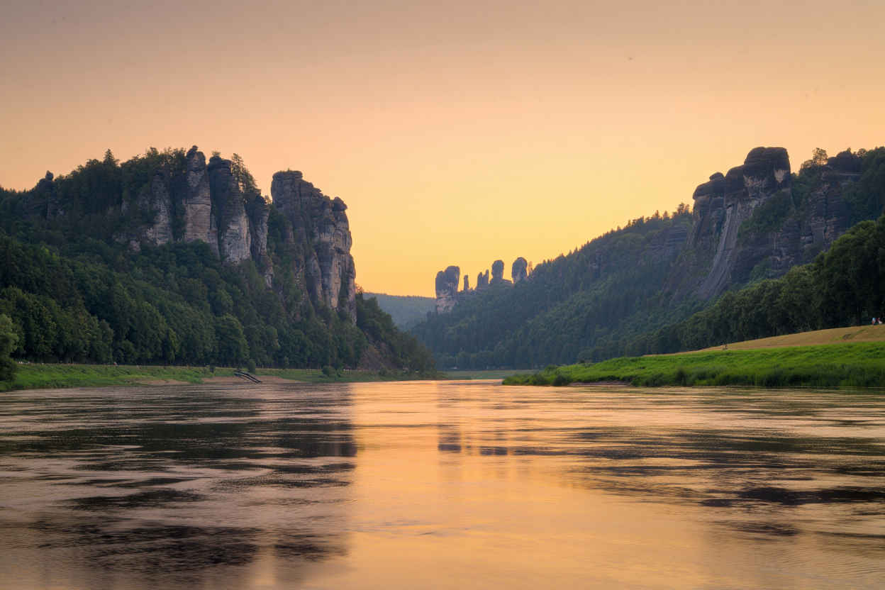 Die Elbe bei Sonnenuntergang mit weiten Wiesen und dem Elbsandsteingebirge im Hintergrund
